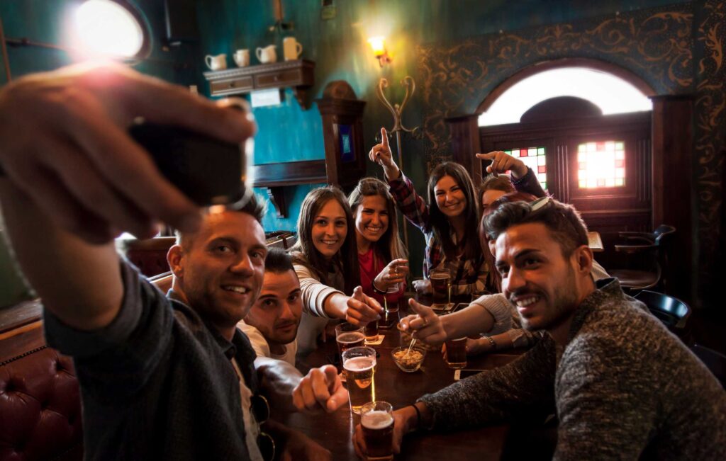 Group of friends around a pub table raising glasses for a toast, smiling at the camera.